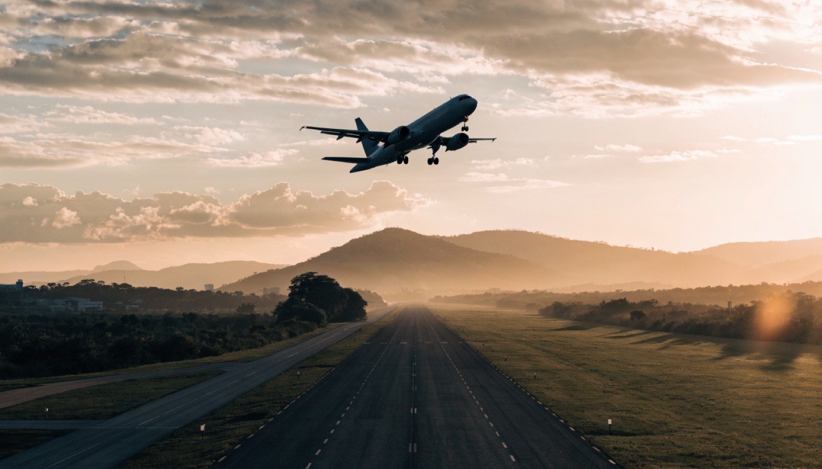 Avião decolando ao entardecer, com montanhas ao fundo