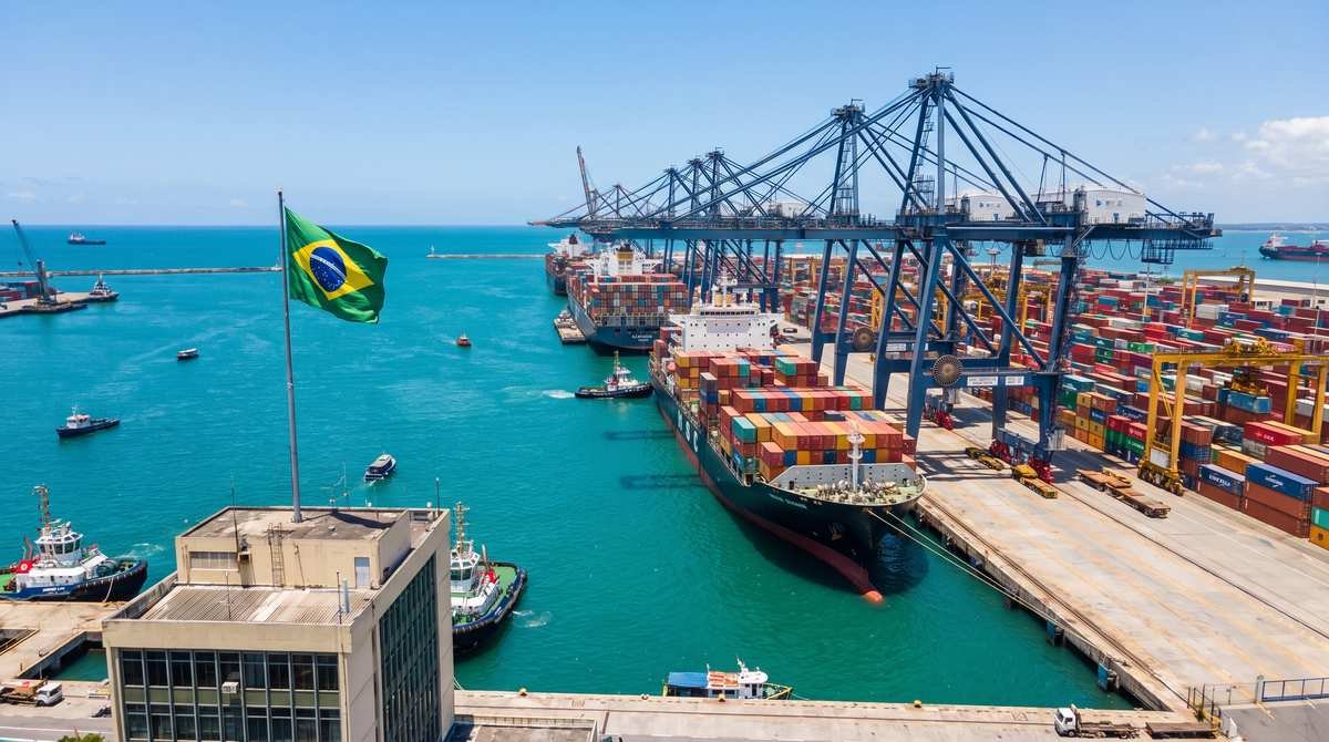 Porto brasileiro movimentado, com navios porta-contêineres, guindastes e bandeira do Brasil hasteada