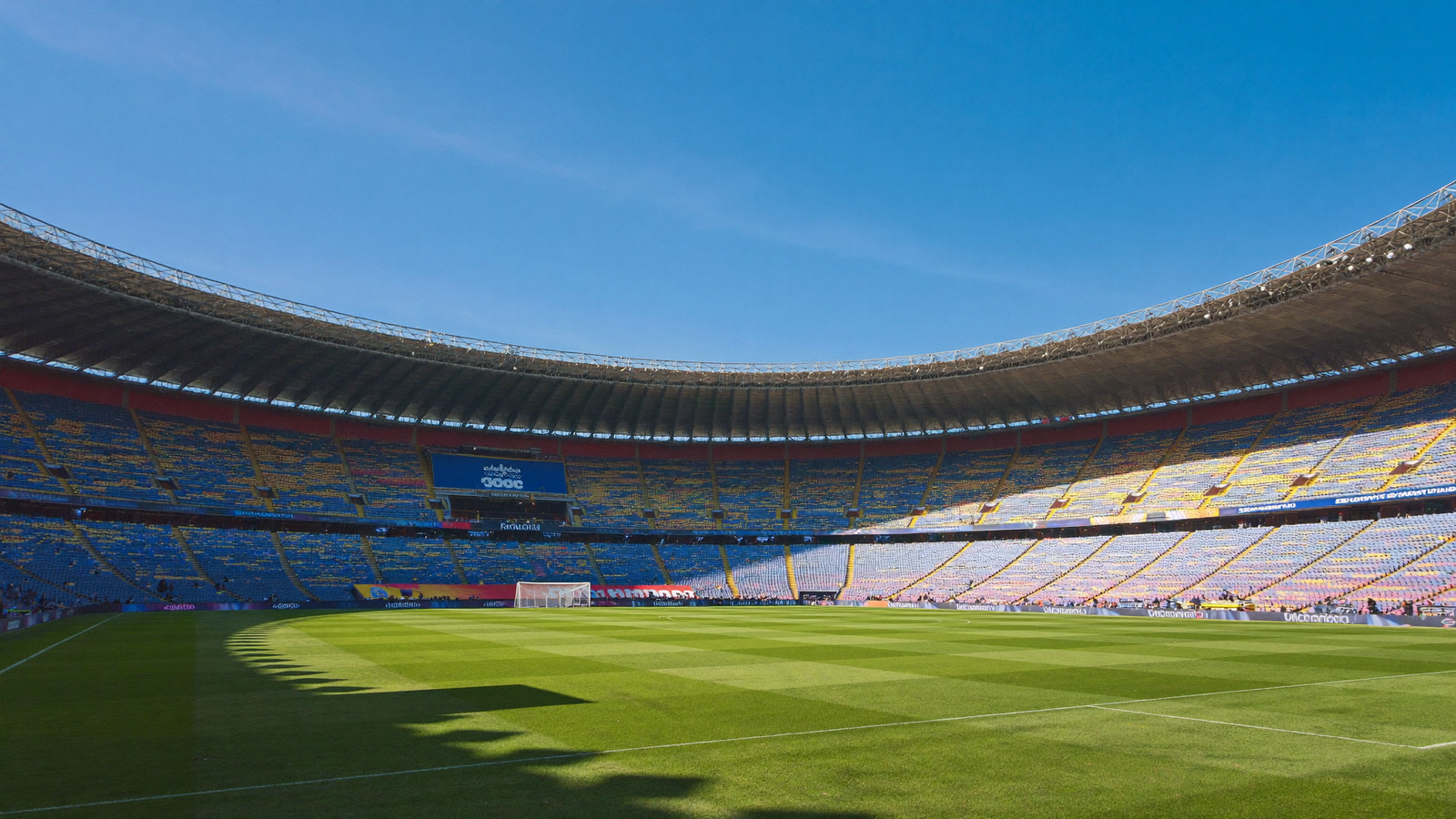 Estádio de futebol iluminado por luz natural, gramado verde e arquibancadas ao fundo em dia ensolarado