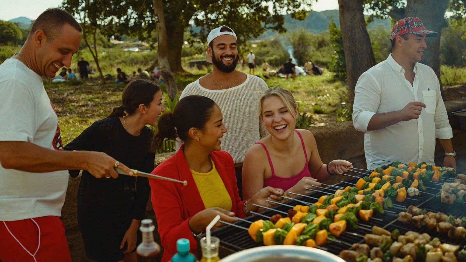 Grupo de amigos reunido em churrasco ao ar livre, preparando espetos na grelha