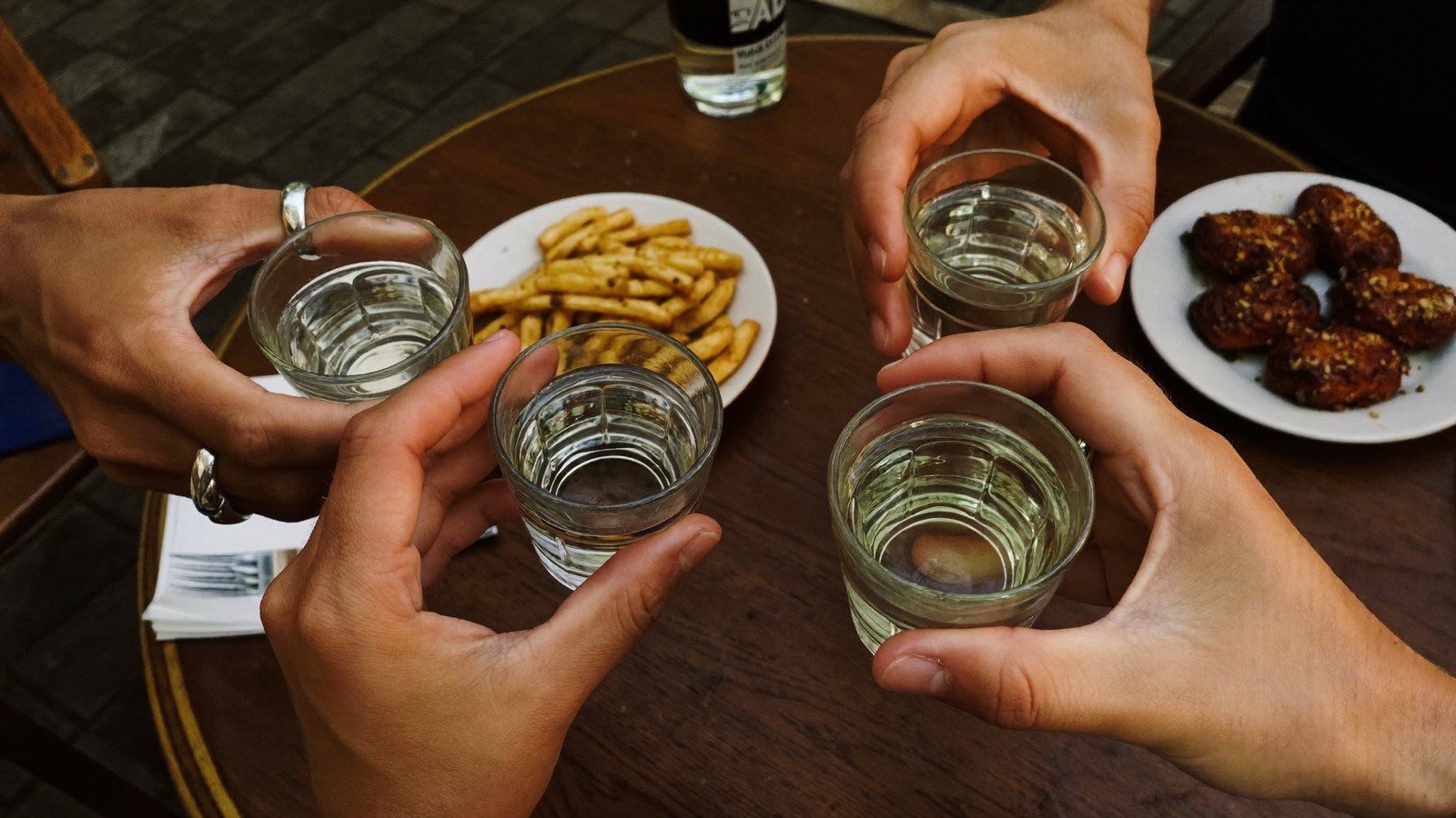 Amigos brindando com copos de cachaça em mesa de boteco, com petiscos servidos