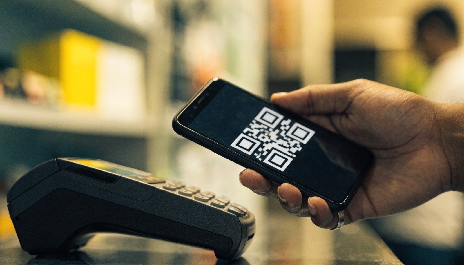 Celular exibindo QR Code de pagamento sendo aproximado de maquininha