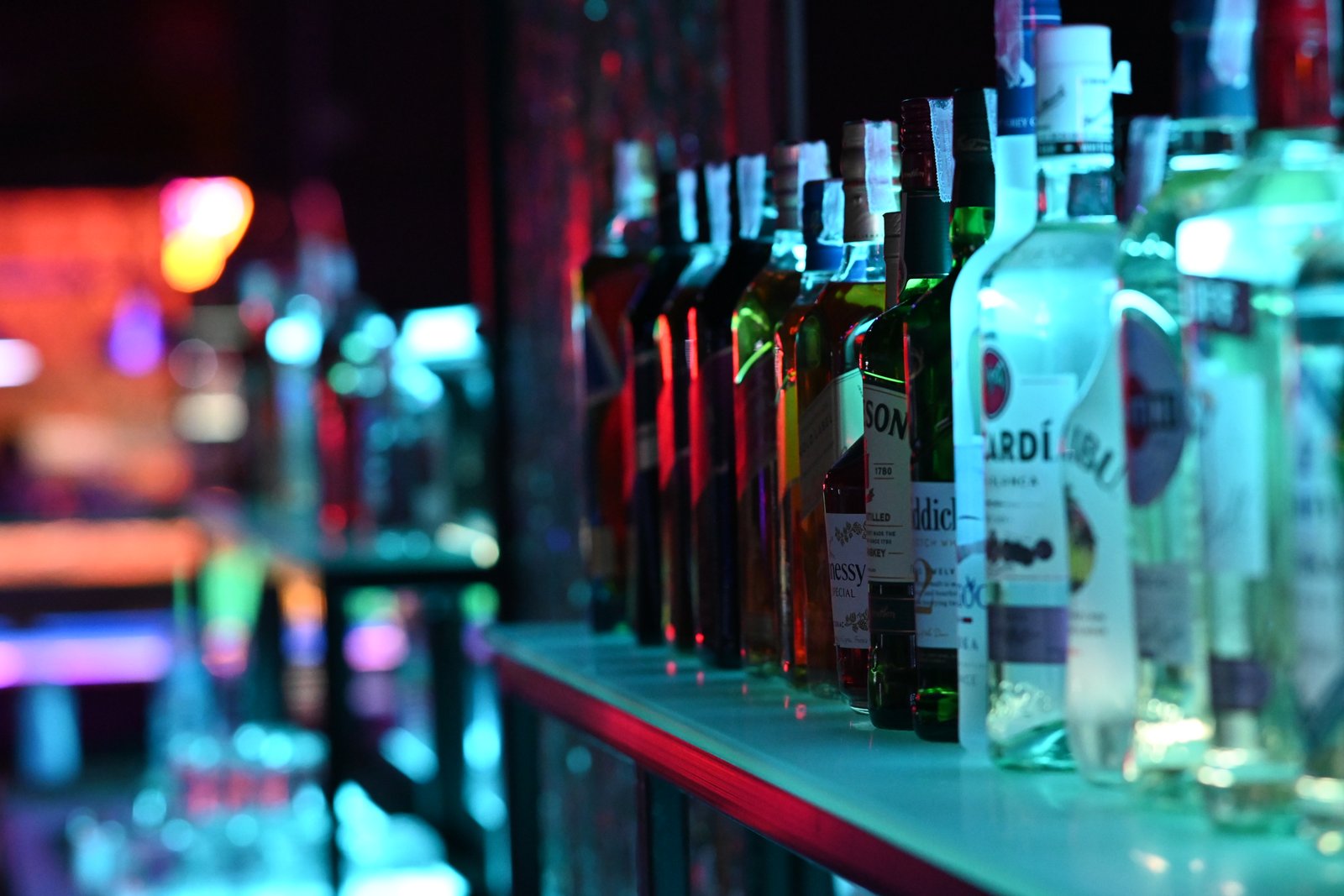 Fileira de garrafas de bebidas em prateleira de bar sob luzes coloridas de neon (Foto: PattayaPatrol/Wikimedia Commons, CC BY-SA 4.0)