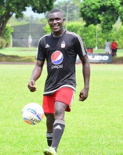 Jovem jogador de futebol sorridente, com bola nos pés, em campo durante treino ao ar livre