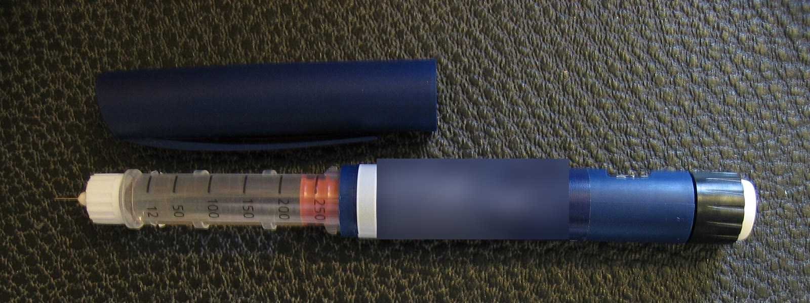 Caneta injetora sobre fundo escuro, do tipo usado para aplicar medicamentos sob a pele, com o rótulo desfocado (Foto: PerPlex/Wikimedia Commons, domínio público)