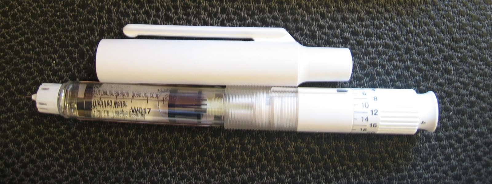 Caneta injetora branca sobre fundo escuro, do tipo usado para aplicar medicamentos sob a pele (Foto: PerPlex/Wikimedia Commons, domínio público)