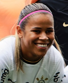 Vic Albuquerque, jogadora do Corinthians, sorri em campo com o uniforme branco e preto do clube