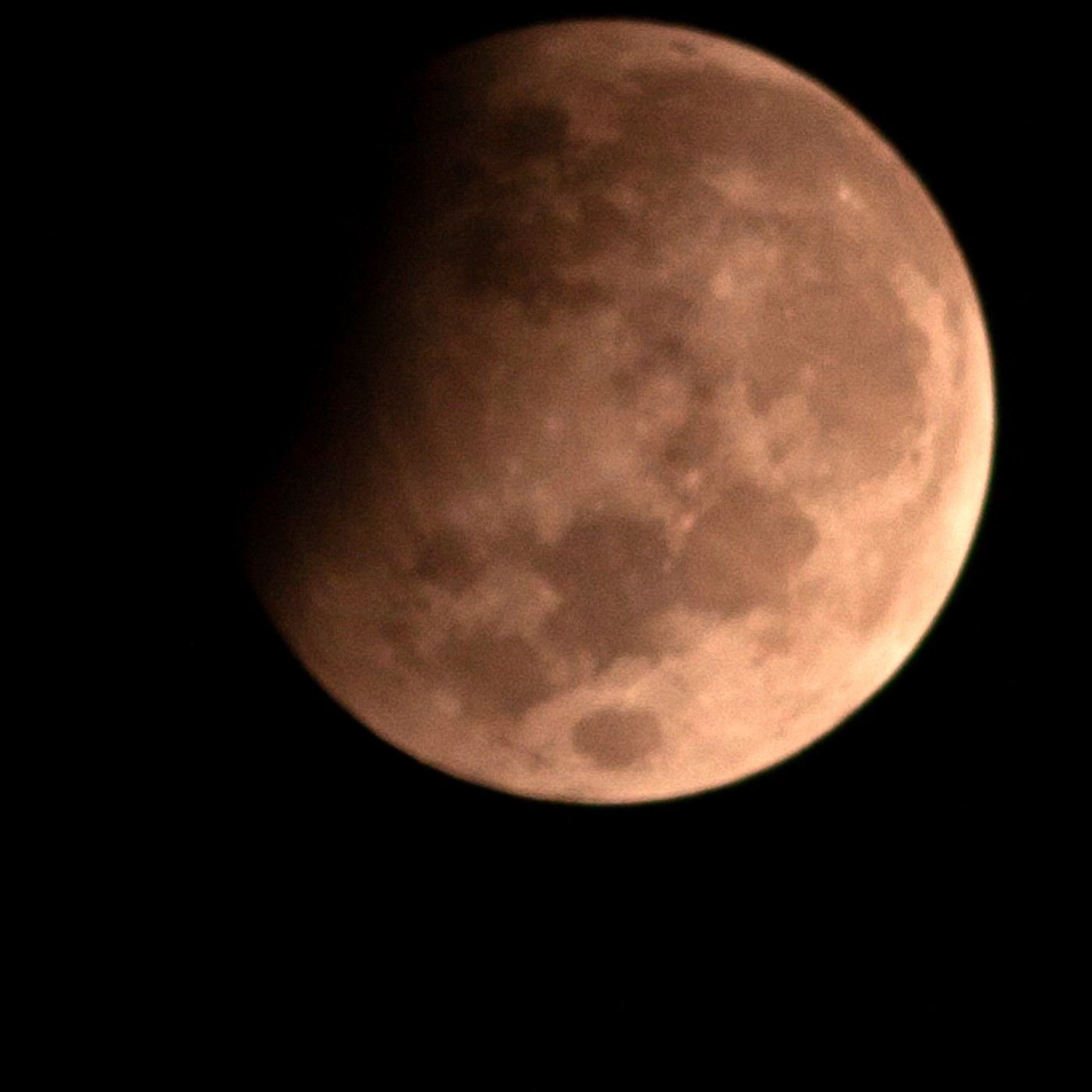 Lua parcialmente eclipsada em tom avermelhado-alaranjado, com parte do disco lunar escurecida pela sombra da Terra