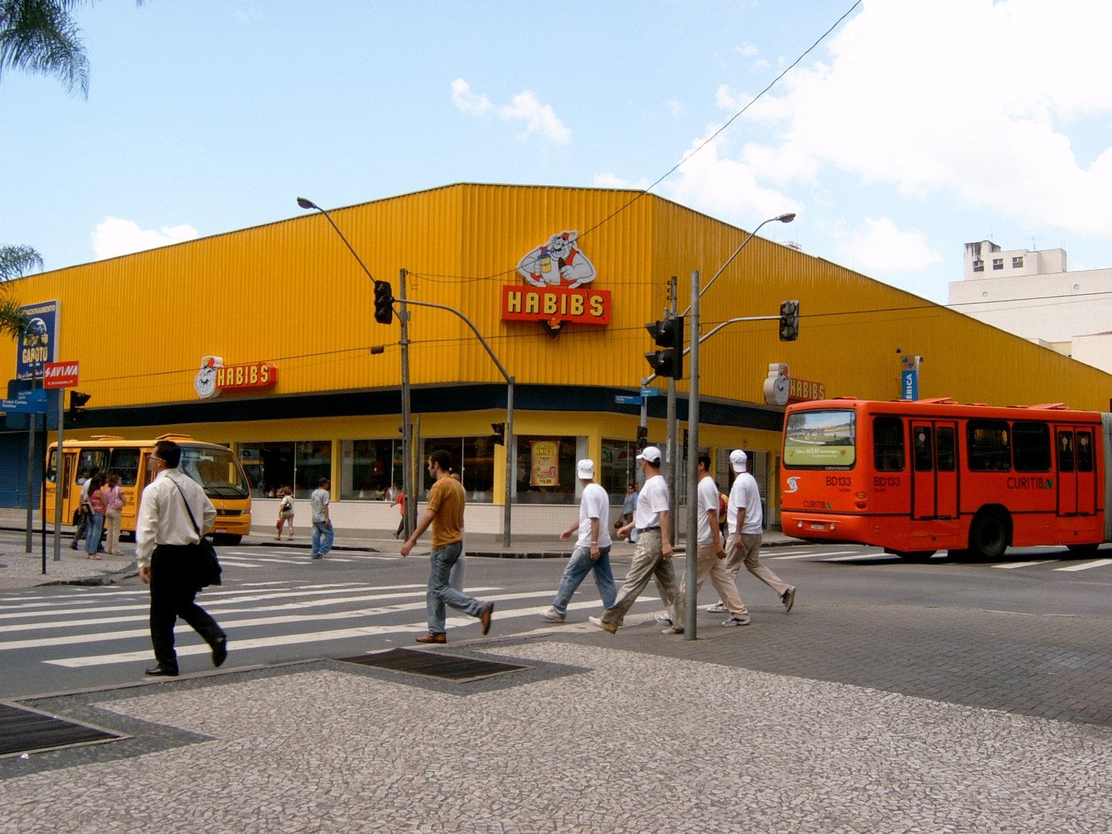 Fachada de uma loja do Habib's em esquina movimentada, com letreiro amarelo e pedestres atravessando a faixa