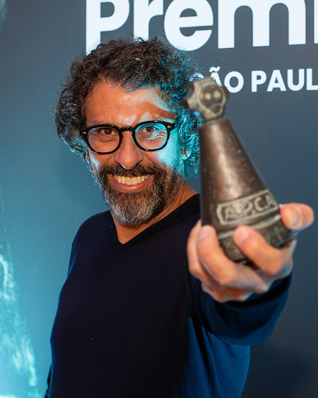 Milhem Cortaz sorrindo com troféu do Prêmio APCA (Foto: amigosdaarte/Wikimedia Commons, domínio público)