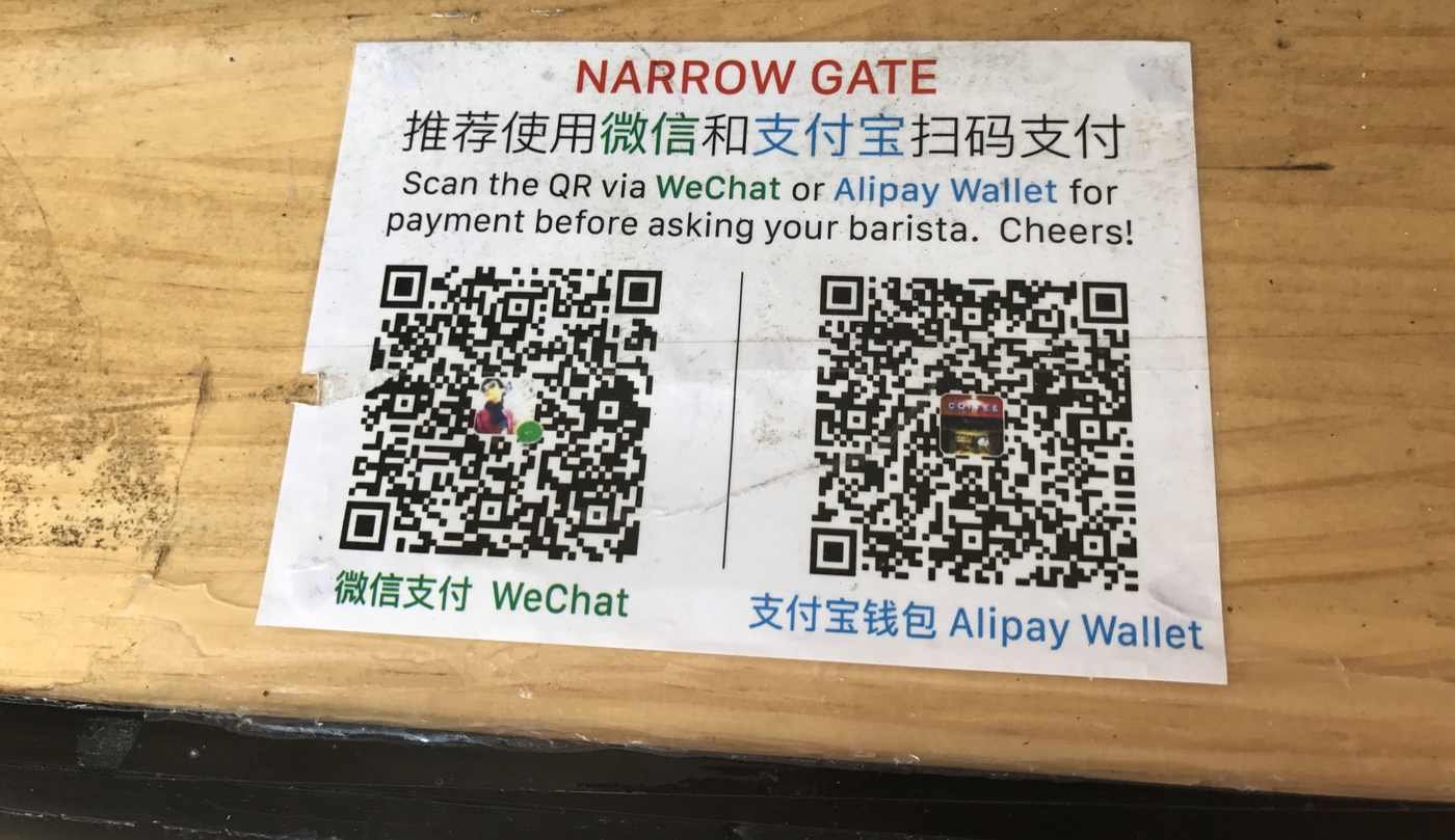 Cartaz com dois QR Codes de pagamento colado sobre o balcão de uma loja, o tipo de código que golpistas cobrem com adesivos falsos (Foto: Harald Groven/Wikimedia Commons, CC BY-SA 2.0)