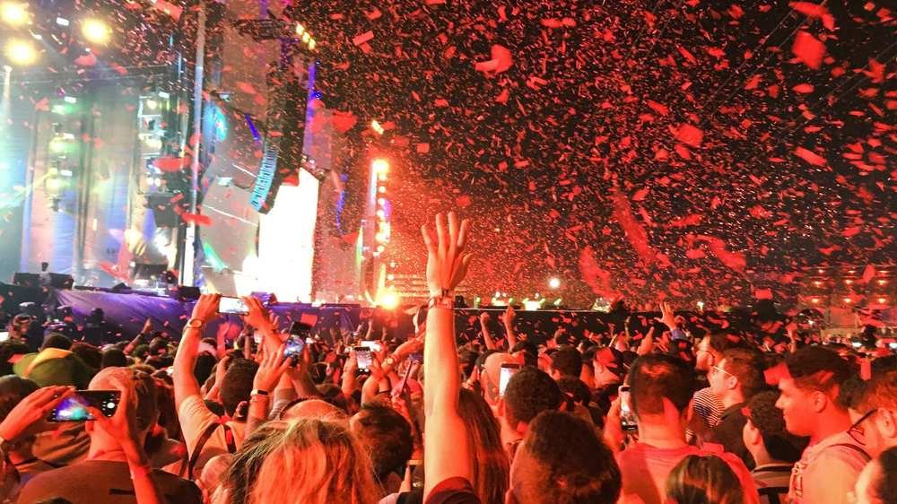 Público de braços erguidos diante do palco do Rock in Rio, sob chuva de confete vermelho