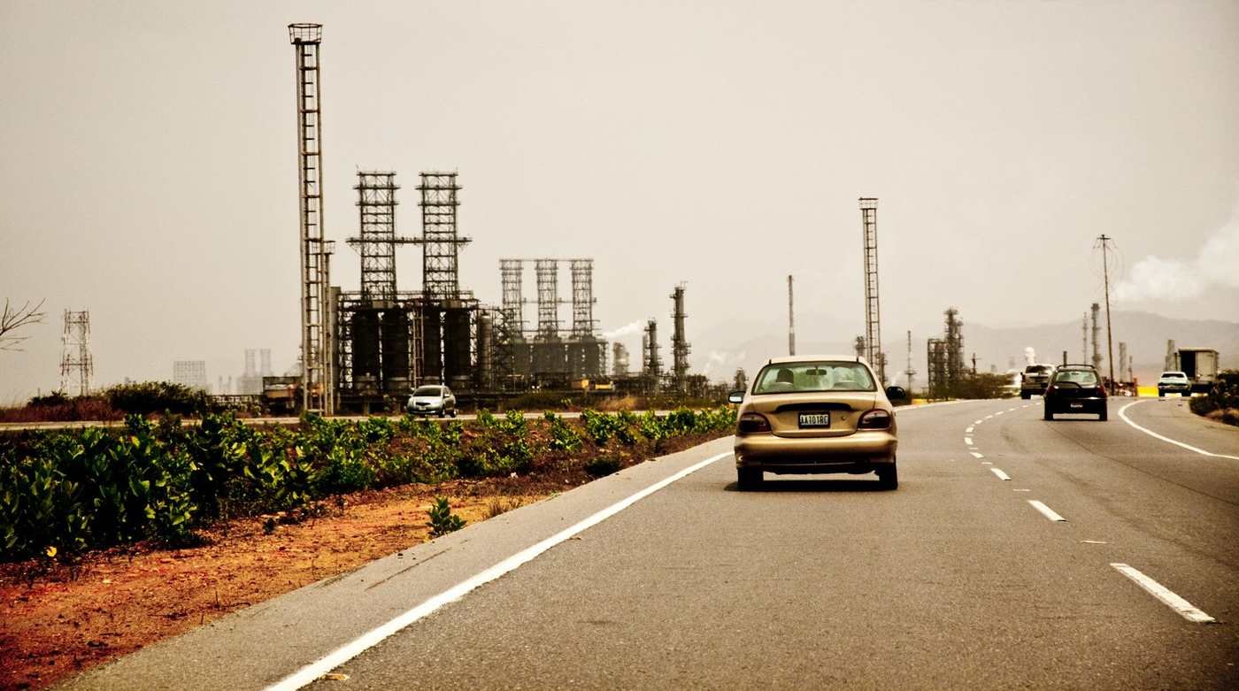 Refinaria de petróleo da PDVSA vista de uma rodovia na Venezuela, com torres industriais ao fundo sob luz de dia
