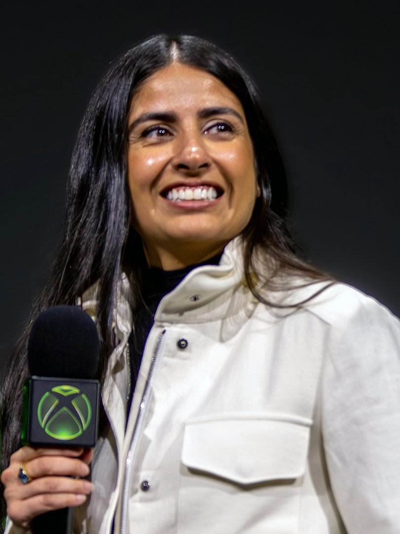 Asha Sharma, CEO da Xbox, sorrindo e segurando um microfone com o logo da Xbox durante evento da marca